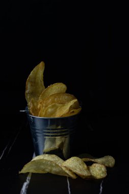 Siyah arka planda, kovada patates cipsi.