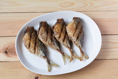 Ahşap zemin üzerinde beyaz tabakta kızarmış uskumru.