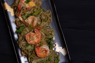 Yakisoba, yeşil çay eriştesi, kızartılmış, siyah arka planda karidesler, düz uzanmış.