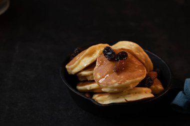 Siyah arka planda siyah bir tavada bal bademi üzümlü krep..