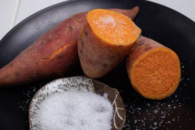 Beyaz arka planda siyah bir tabakta kaynatılmış tatlı patates.