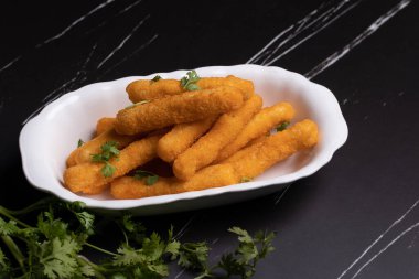 Tavuk nugget çubukları siyah arka planda bir fincanda.