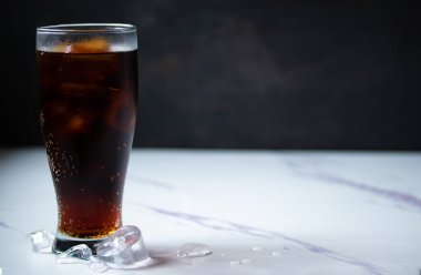 Siyah arka planda berrak bardakta kola içilir.