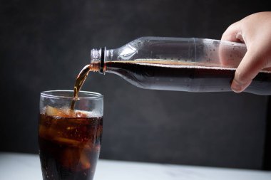 Bir şişe kolayı temiz bir bardağa tutarken.