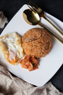 Siyah arka planda beyaz tabakta kızarmış yumurtalı kimchi marulu pilav.