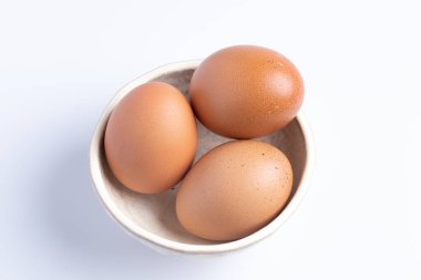 Beyaz arka planda bir fincanda üç taze yumurta..