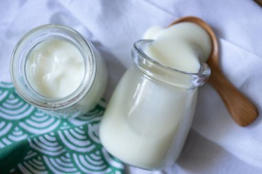 Yeşil arka planda iki cam kavanozda beyaz yoğurt.