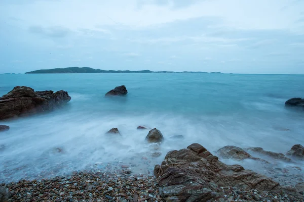 Dreamy wave crashing on rocky beach in twilight time on the sky 
