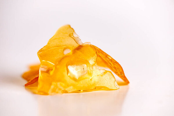 Macro detail of cannabis oil concentrate aka shatter isolated over white background