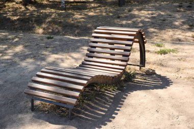 Tahtalardan yapılmış eğri bir ahşap tezgah boş bir yaz parkında duruyor.