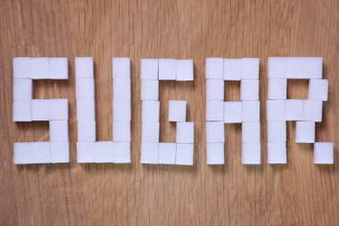 Tahta kahverengi arka planda rafine şeker küpleri ile kaplanmış şeker kelimesi