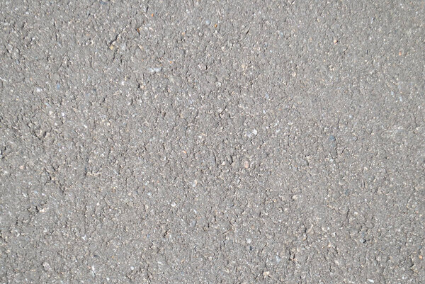 The texture of the asphalt on the road in a light shade illuminated by the sun for the whole frame, gray and grungy