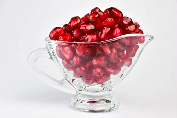 Dans un bol en verre transparent sont versés juteux rouge vif graines de fruits de grenade. Sur fond blanc — Photo