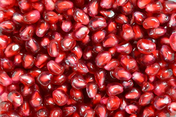 The whole background is covered with juicy bright red pomegranate fruit grains. Shot close-up — Stock Photo, Image