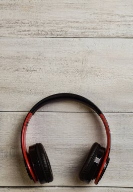 Siyah ve kırmızı kablosuz kulaklıklar çerçevenin altındaki bej ahşap bir masanın üzerinde duruyor.