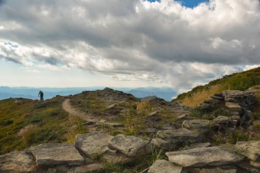 Dağlık kayalık bir dağ. Dağılmış taşlar. Uzaktan bir bisikletçinin indiği bir dağ. Gökyüzünün arka planında bulutlarla