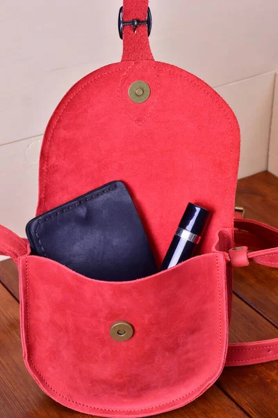 On a wooden background, a womans leather red bag is open, she has a purse and lipstick — Stock Photo, Image