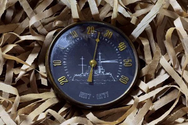 An old vintage street thermometer in a circular shape with an analogue circular operating dial rests on intertwined paper strips