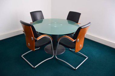 Dört boş deri dekoratif ofis sandalyesi, tahta sırtlı cam yuvarlak bir masanın etrafında oturuyor. Yan görünüm