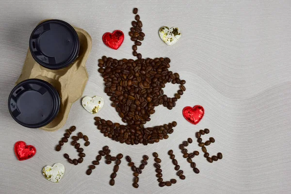 This figurine in the form of a cup of coffee with a saucer is made of coffee beans with the inscription COFFEE IS MY LIFE under it. On the left are two disposable coffee cups and decorative hearts