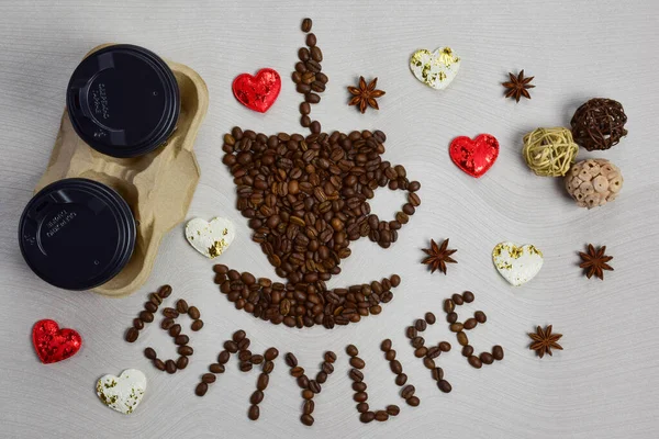 This figurine in the form of a cup of coffee with a saucer is made of coffee beans with the inscription COFFEE IS MY LIFE under it. On the left are two disposable coffee cups and decorative hearts