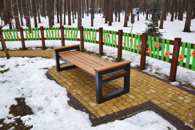 Kış parkında boş bir dekoratif bank var, arkasında çok renkli küçük bir çit var.