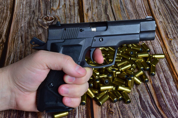 A pile of traumatic cartridges was piled on a wooden background. Against their background, a hand holds a pistol