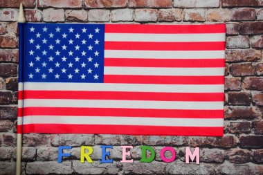 FREEDOM kelimesi, bayrak direğinde bayrak direğinin altında eski bir tuğla duvarın arka planında yer alan çok renkli harflerle doludur.