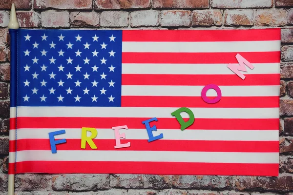 Freedom 这个词用五颜六色的字母在美国国旗上一条弯曲的线衬托在一面古老的砖墙后面 — 图库照片