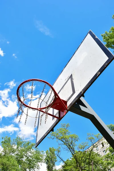 Μπάσκετ στεφάνι και backboard κατά ένα φωτεινό μπλε ουρανό με λευκά σύννεφα. Πυροβολισμός από κάτω — Φωτογραφία Αρχείου