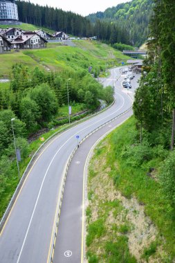 Yazın bir kayak merkezinde boş asfalt yol. Yüksek bir açıdan bak. Arka planda çok güzel tatil evleri var.