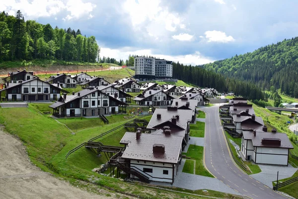 Estación de esquí en verano con filas de casas bajas con techos marrones sobre el telón de fondo de un cielo azul brillante y montañas — Foto de Stock