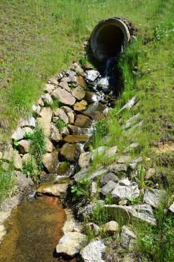 Tepedeki büyük beton bir borudan, taşlardan yapılmış özel bir oluk boyunca akan ve suyu akan bir pınar.