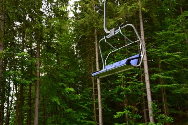 Mavi kayak asansörünün boş bir bank orman ağaçlarının arka planına karşı dağdan iner. Yazın bir kayak merkezinde çekilmiş.