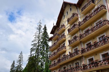 Bina, gökyüzü ve ağaçların arka planına karşı balkonları olan çok katlı büyük bir oteldir. Resimde hiç insan yoktur, sol tarafa metin eklemek için bir yer vardır.