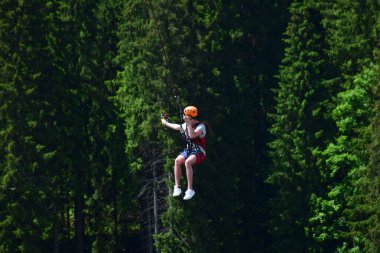 Miğferli genç bir adam bungee jumping 'den atladı ve şimdi bir ipe tutunuyor, yeşil bir ormanın bulanık arka planına karşı kendini bir spor kamerasında sallıyor ve filme çekiyor.