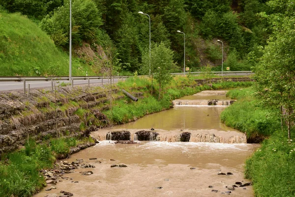 Брудний потік води в річці з дрібними водоспадами біля дороги через затоплення — стокове фото