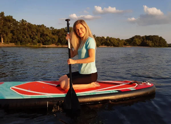 美丽的姑娘坐在Sup的船桨上 划着飘扬在河流和森林后面的桨 — 图库照片