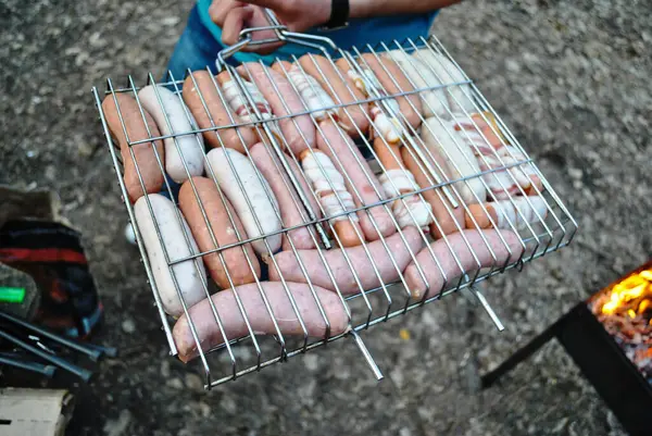 Różne rodzaje kiełbasek z mięsem smażone są na ognisku w lesie. — Zdjęcie stockowe