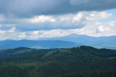 Dağın tepesinden vadinin manzarası birkaç ormanlık dağın arka planına ve bulutlu gökyüzüne karşı.