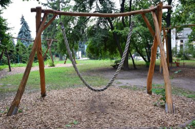 Kalın ipten yapılmış dekoratif büyük ahşap salıncak. Eğlence için bir yaz parkının arka planına karşı.