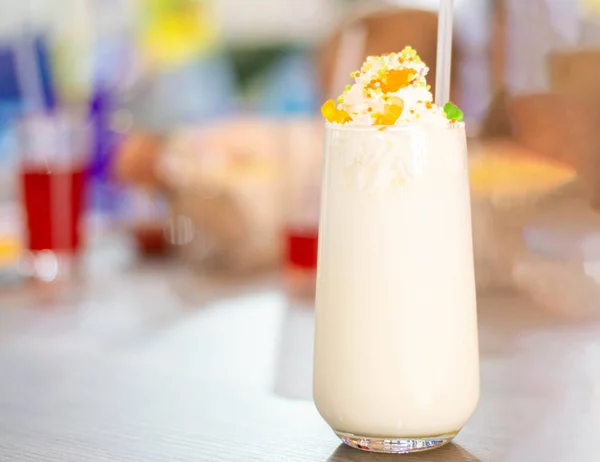 A baby milkshake, with whipped cream and sprinkles, sits on a wooden table in a cafe. Side view, space for text, The concept of summer childrens recreation.