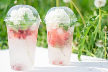 Karpuz dilimleri ve beyaz çiçekli plastik bardakta buz küpleriyle kokteyl. Beyaz ahşap bir arka planda, çimlerin üzerinde. Yaz tropik ferahlatıcı içeceği.