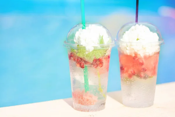 Karpuz dilimli kokteyl ve çiçekli plastik bardaklarda buz. Beyaz bir arka planda, tatil köyü havuzunun kenarında. Lüks tatil kavramı. Açık havuz geçmişi. Yatay.