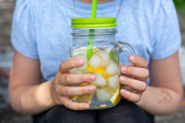 Yazın küçük, güzel, beyaz elbiseli bir kız dışarıda soğuk limonata içiyor. Saçları açık gülümseyen bir kızın portresi..