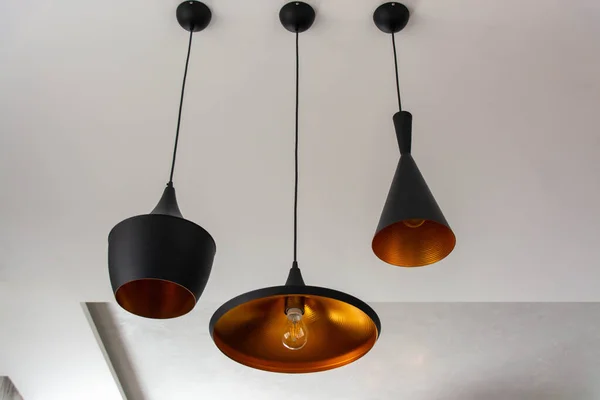 Three hanging lamps in black color in the style of an industrial loft in the interior.