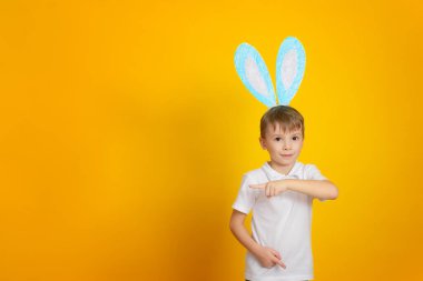 Paskalya tatili beklentisiyle tavşan kulaklı şirin bir çocuk. Stüdyo portresi, sarı arka planlı konsept. Boşluğu kopyala