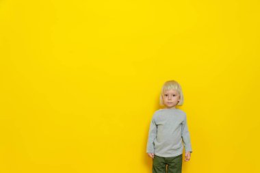 Yakışıklı bir çocuk sarı bir arka planda duruyor. Onun uzun beyaz saçları var. Stüdyo resmi.