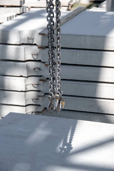 Metal bars on slings made of chains against the background of reinforced concrete products