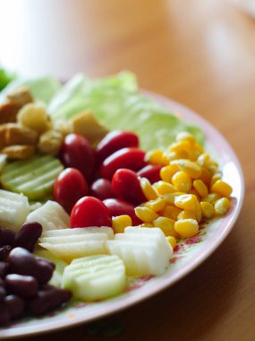 Meyve salatalarının ön planda sarı mısırları ve arka planda domates ve havuç gibi bulanık kısımları vardır..